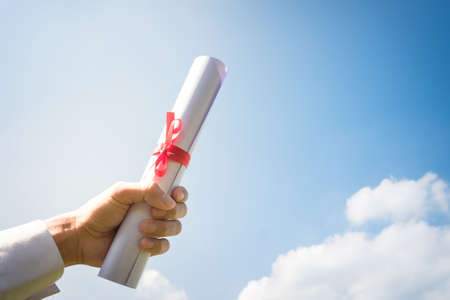 Hand holding Graduation certificate roll under the sunshine, blue sky background.の写真素材