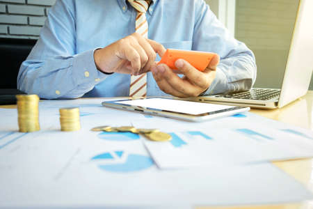 businessman using calculator with stacked coins arranged at office desk and many document data graph in morning light, business concept.の写真素材