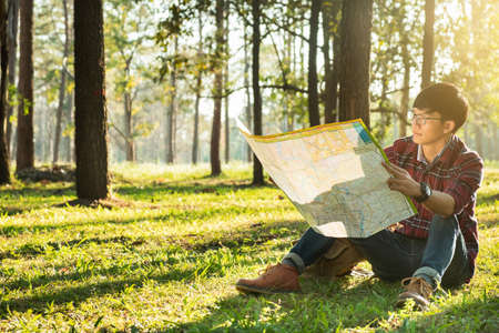 Young Man Traveler with backpack sitting looking at the map relaxing outdoor on background Summer...