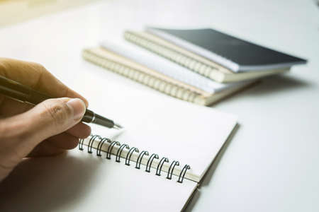 Close-up human hand writing something on paper notebook in sunlight background.の写真素材