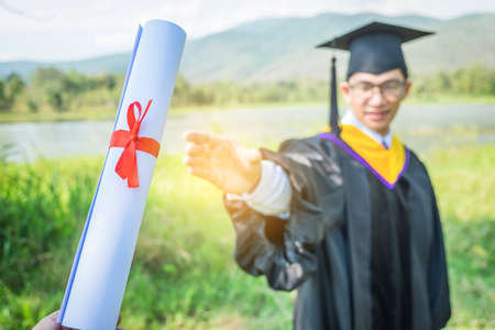 Graduation: Student standing up and smile holding Graduation certificate with Diploma With background in the nature.の写真素材
