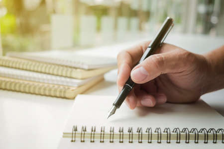 Close-up human hand writing something on paper notebook in sunlight background.の写真素材
