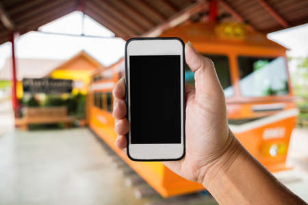 right hand holding using smartphone with black screen on Abstract blur background of trainstation.の写真素材