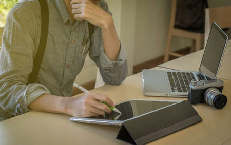 Close-up of male hand, using digital tablet, computer and camera while sitting at his working place.の写真素材