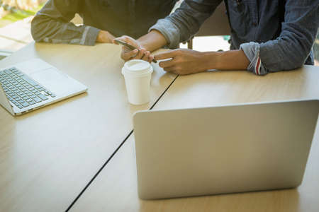 Close-up of male hand, using phone and computer while sitting at his working place.の写真素材