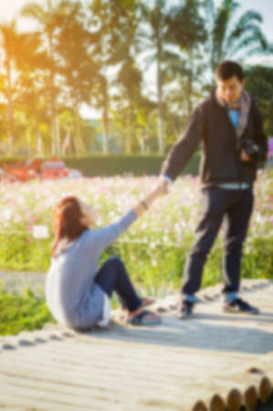 The boys are helping pull the woman up in flower garden under sunshine, blurred background.の写真素材