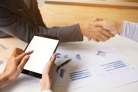 Teamwork process, Close-up of two business people shaking hands while sitting at the working place.の写真素材