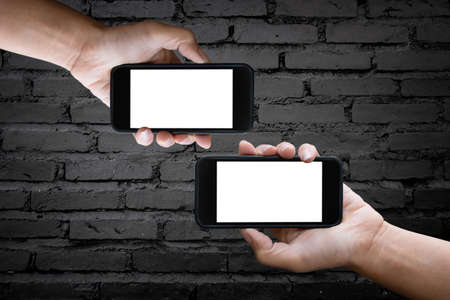 Two hands holding blank screen of a smartphone at the old black brick wall.の写真素材
