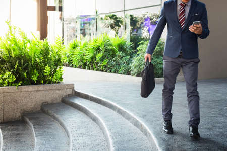 Businessman walking on the stairs and using smartphone outdoors.の写真素材
