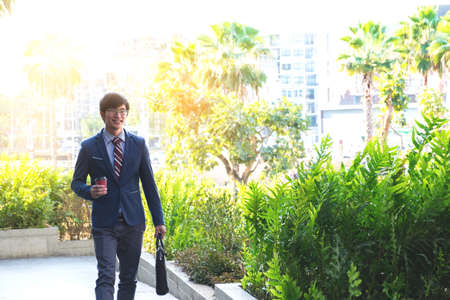 picture of a young business man walking forward with a briefcase in one of his hands and coffee cup.の写真素材