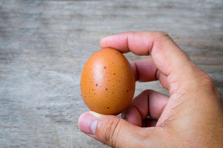 Close-up of hand is catching egg on wooden background.