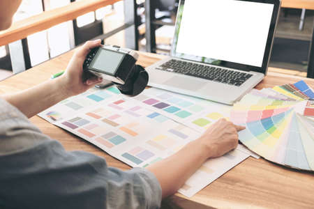 Color samples, colour chart, swatch sample, Graphic designer being selecting Color band and graphics tablet at workplace with work example in camera and laptop on wooden desk.の写真素材
