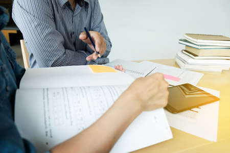 Education, teaching, learning, technology and people concept. Two high school students or classmates with helps friend catching up workbook learning in classroom, Tutor books with friends.の写真素材