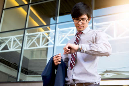 Executive in a hurry, businessman looking at his watch on hand, checking the time while standing on the office. outdoor background.の写真素材