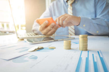 businessman using calculator with stacked coins arranged at office desk and many document data graph in morning light, business concept.の写真素材