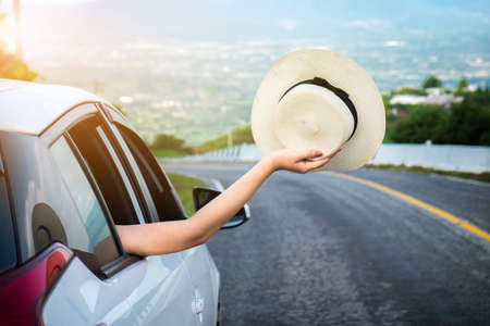 Relaxed happy traveler, Young beatiful asian gilr holding hat weave and Reach out of the car at sunset and beautiful view with mountain road background.の写真素材