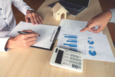 Man sign a home insurance policy on home loans, Agent holds loan investment chart graph documents, pointing and calculating table installment payment, Real Estate concept.の写真素材