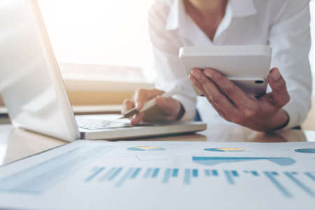 Female accountant calculations and analyzing financial graph data with calculator and laptop...