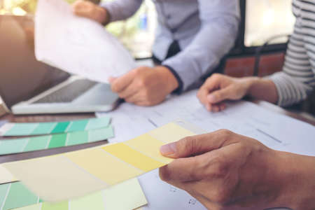 Two colleagues interior Creative creativity graphic designer working with graphics laptop, blueprint and colour chart at workplace on wooden desk , colour ideas style concept.の写真素材