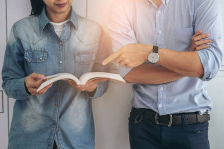 Cheerful young student standing holding book and reading, classmates helps friend catching up workbook and learning tutoring lean on locker, teaching, learning, People, Education and school concept.の写真素材