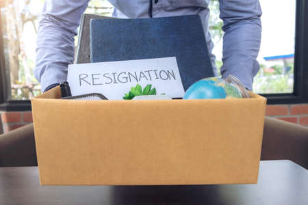 Businessman carrying packing up all his personal belongings and files into a brown cardboard box to resignation, resign concept.のeditorial素材