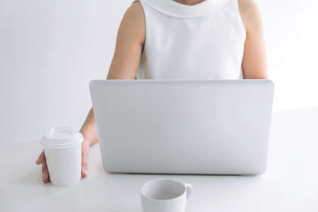 young woman working indoors at a modern office holding a coffee cup while using her laptop.の写真素材