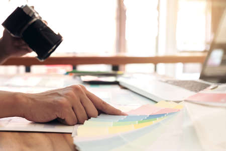 Color samples, colour chart, swatch sample, Graphic designer being selecting Color band and graphics tablet at workplace with work example in camera and laptop on wooden desk.の写真素材