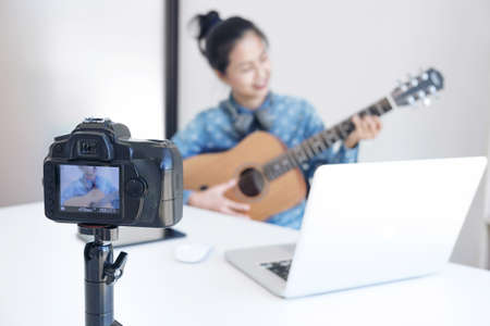 social media learning concept, relaxing and playing guitar, Young woman concentrating learn and play the guitar to a tutorial on lesson online, while she recording music video in camera at home.の写真素材