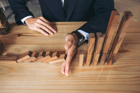 Close up of businessman hand Stopping Falling wooden Dominoes effect from continuous toppled or risk, strategy and successful intervention concept for business.の写真素材