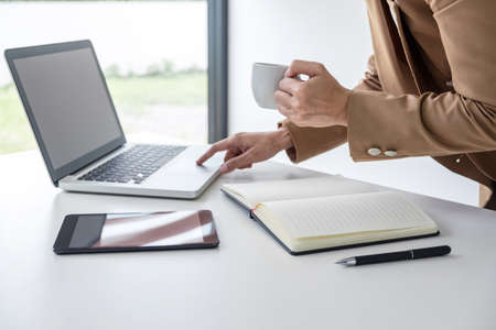 Young Entrepreneur woman manager working indoors at a modern office, typing and holding a coffee cup while using her laptop.の写真素材