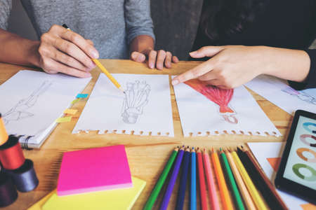 Two young dressmaker or designer colleagues working as fashion designers and drawing sketches for clothes, choose color bar in tablet, profession and job occupation, Fashion Designer Stylish Concept.の写真素材