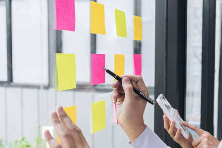 Young creative professional leader using post it notes in glass wall to writing strategy business...