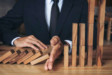 Close up of businessman hand Stopping Falling wooden Dominoes effect from continuous toppled or risk, strategy and successful intervention concept for business.の写真素材