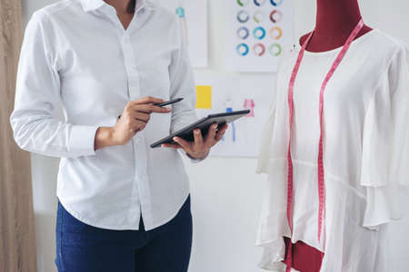 Stylish fashion designer working with measure red dummy as sketches in digital tablet of new...