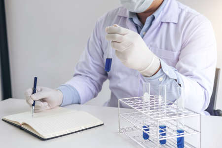 Scientist or medical in lab coat holding test tube with reagent, mixing reagents in glass flask in...