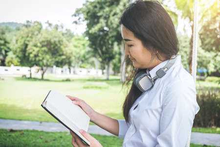 smiling young woman reading the book and sitting on the grass in autumn park.
