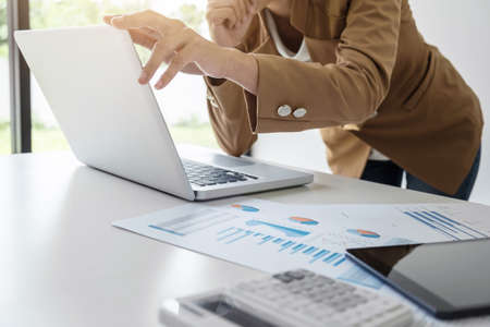 Elegant businesswoman leader working on laptop in a modern office, analyzing data and graph, using calculator calculate, young attractive woman typing on computer at white table.の写真素材