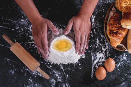 Raw for bread with ingredients on black background, male hands kneading sprinkled with flour table.