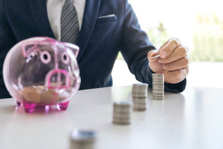 Businessman using calculator to analysis business investment and stacking coins arranged at office desk and piggy bank in modern office, financial concept.の写真素材