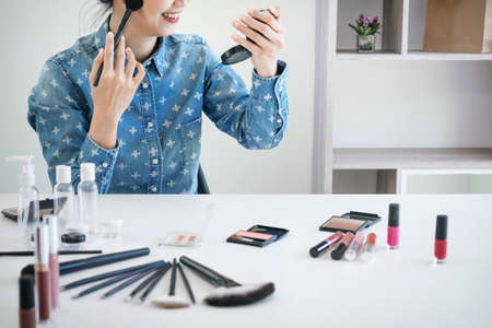 Happy smiling elegant woman or beauty blogger with brush on recording video while review product make up tutorial for theme about video blogging on camera screen.の写真素材