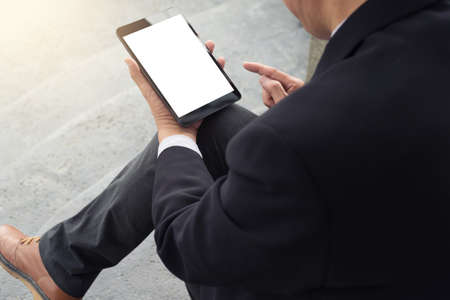 Attractive Confident businessman sitting in a black suit and using digital tablet to analyze...