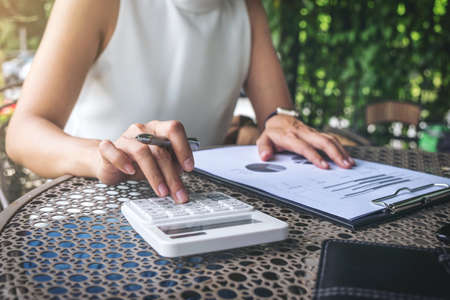 Work and relax, Woman freelancer is working new project of business stragegy plan and using calculator to analysis information data, while sitting garden scenery outdoor background.の写真素材