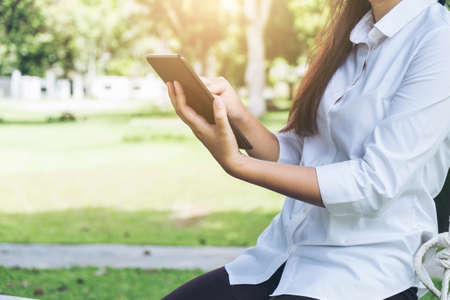 Work and relax, Woman freelancer is working on digital tablet, while sitting garden scenery background.の写真素材
