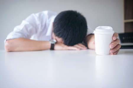 Tired businessman sleeping at work in modern office with hand holding coffee cup, people dozing on workplace.の写真素材