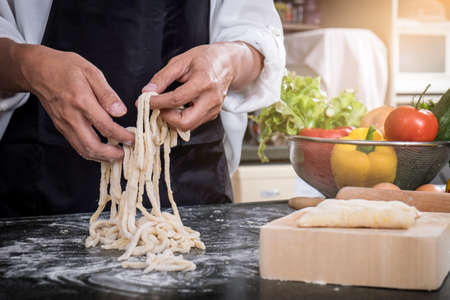 female housewife making homemade pasta with flour and eggs over table in kitchen.の写真素材