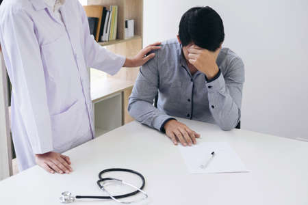 Friendly Professional medical doctor in white uniform coat holding patient hand sitting at the desk for encouragement, cheering and support while listen medical results.の写真素材
