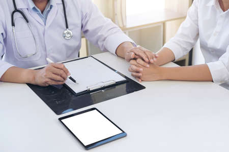 Friendly Professional medical doctor in white uniform coat holding patient hand sitting at the desk for encouragement, cheering and support while listen medical results.の写真素材