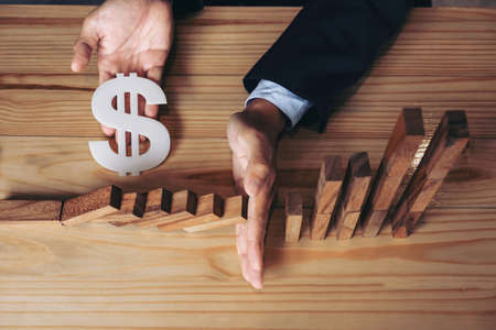 Close up of businessman hand Stopping Falling wooden Dominoes effect from continuous toppled or risk, strategy and successful intervention concept for business.の写真素材