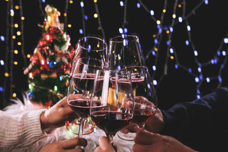 Friends celebrating Christmas or New Year eve party, cheering with wine, christmas lights decoration background, christmas atmosphere.の写真素材