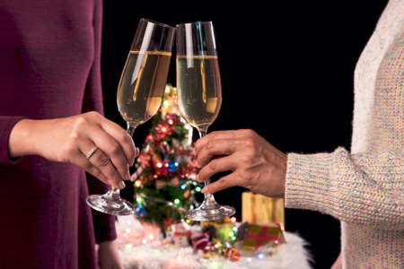 Beautiful two women holding glasses with champagne celebrating Christmas and gift boxes at corporate party and christmas lights, New Year Frame for your text.の写真素材